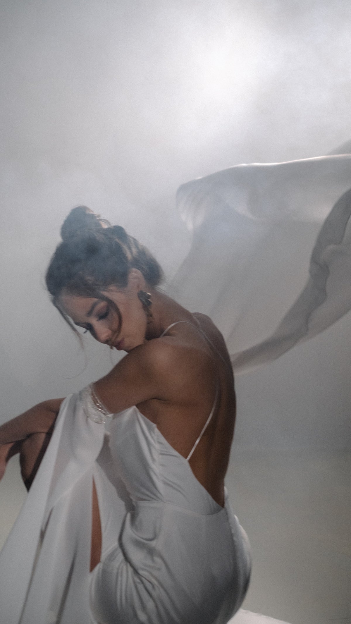 Bride bending forward in haze, open back silk wedding dress with a chiffon sleeve swept up in the air, FEYRE