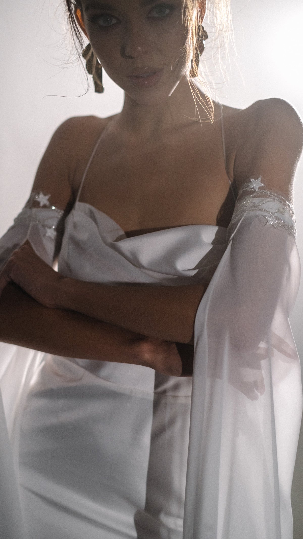 Bride hugging her arms, draped cowl neckline of a silk wedding dress with beaded lace sleeve cuffs, FEYRE