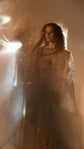 Hazy studio shot with a lens flare, sparkling beige lace wedding dress with draped sleeves, model gazing to the side, Galaxy Champagne 2.0
