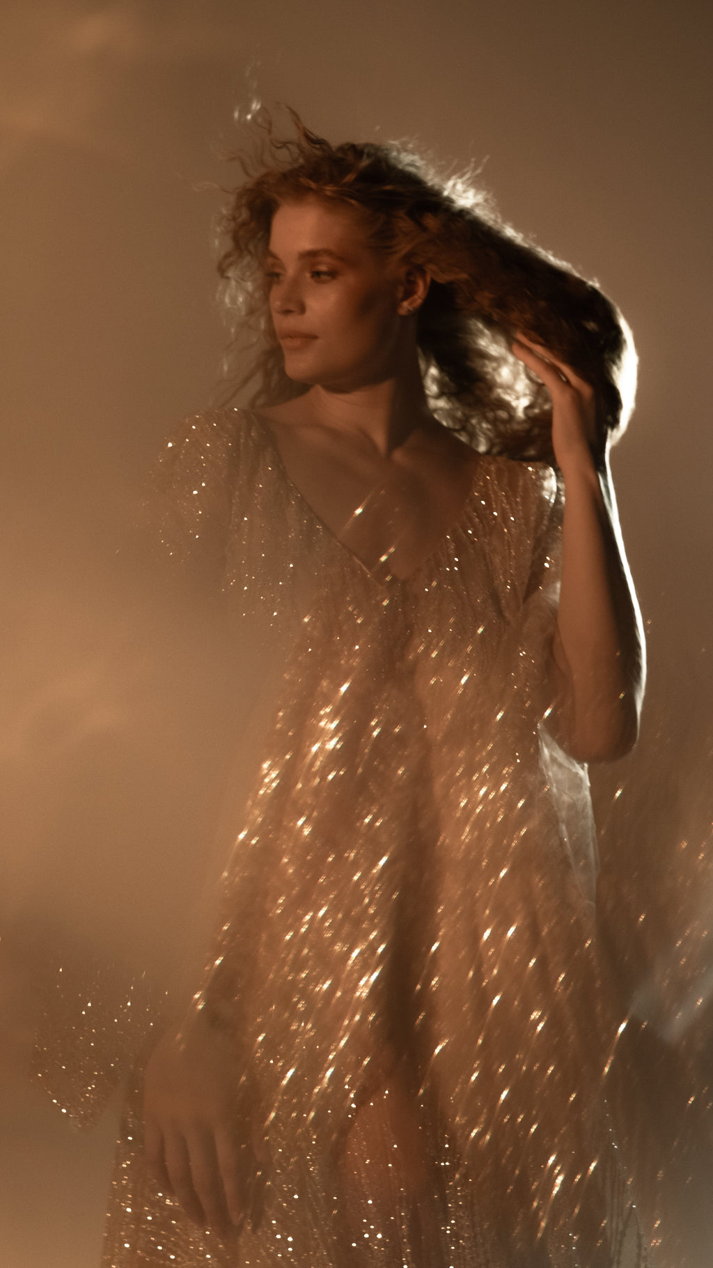 Model with a hand in her hair, glitter lace wedding dress sparkling through soft haze in warm golden light, Galaxy Champagne 2.0