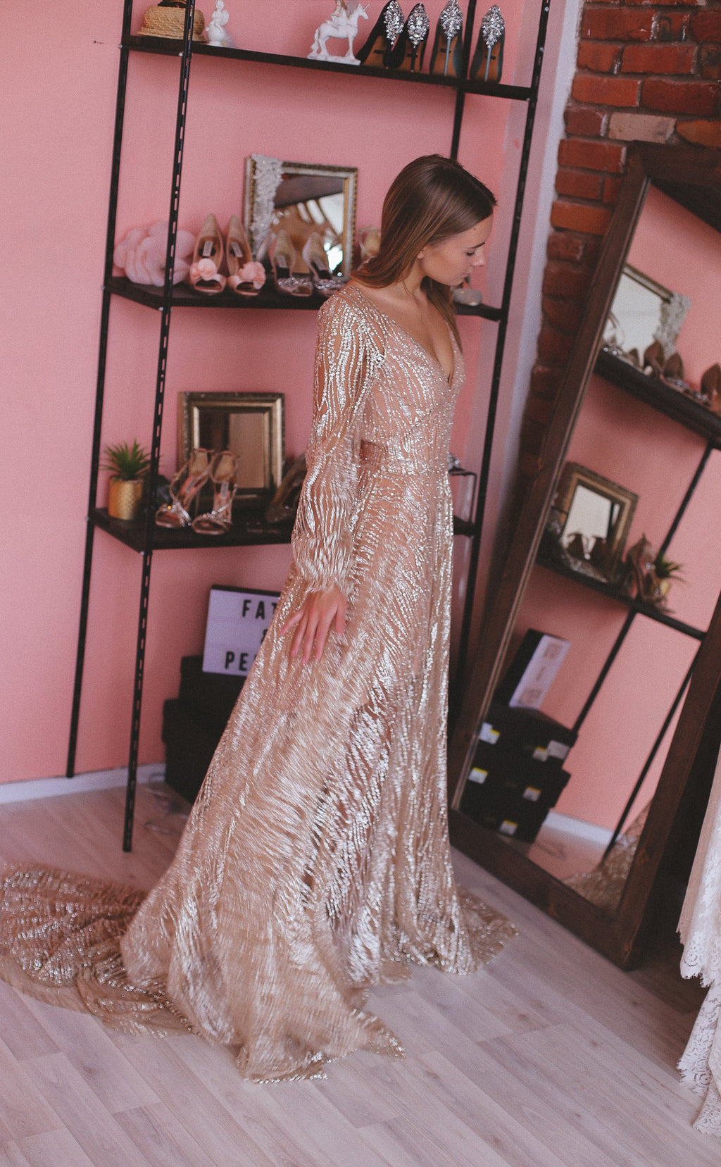 Bride in a pink boutique beside shoe shelves, champagne glitter lace wedding dress with long sleeves and a pooled train, Galaxy Champagne