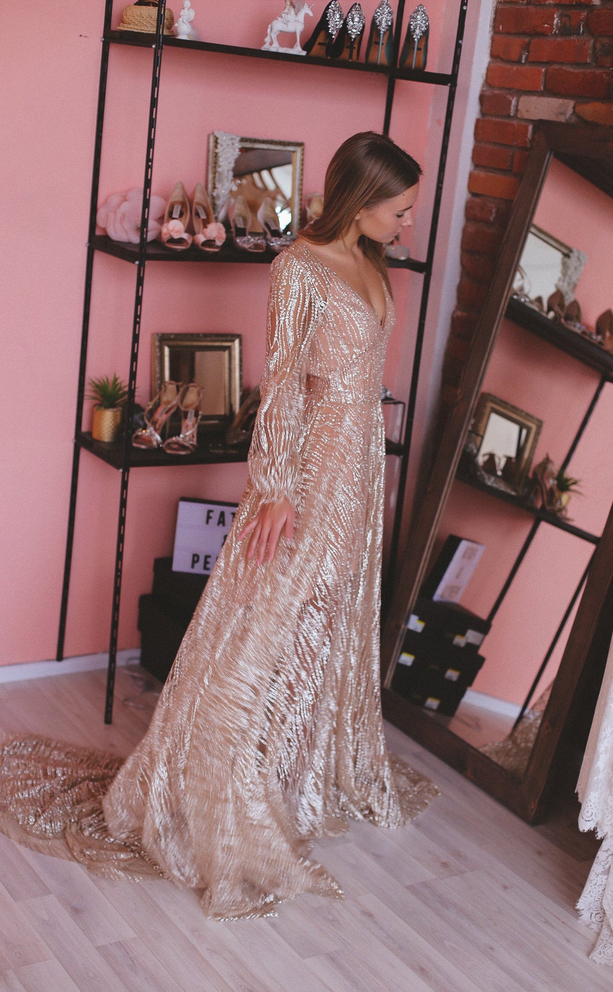 Bride in a pink boutique beside shoe shelves, champagne glitter lace wedding dress with long sleeves and a pooled train, Galaxy Champagne