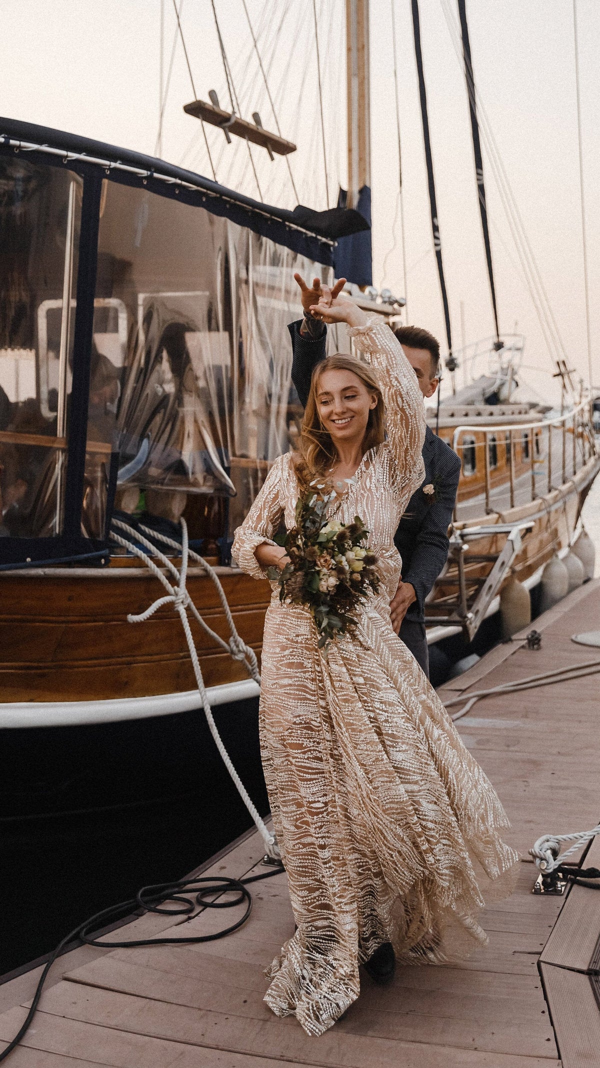 Bride dancing on a boat deck with a bouquet, sparkly champagne lace wedding dress swinging around her feet, Galaxy Champagne