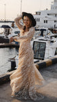 Twirling bride in a black hat at a harbour, long-sleeve beige glitter lace wedding dress flaring at the hem, Galaxy Champagne