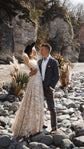 Elopement couple among river stones and pampas grass, bride in a long champagne glitter lace wedding dress and hat, Galaxy Champagne