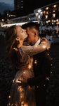 Kiss under fairy lights at night, sheer long sleeves of a champagne glitter wedding dress wrapped around the groom, Galaxy Champagne