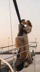 Bride kissing the groom on the bow of a sailboat at sunset, beige glitter lace wedding dress draped over the rail, Galaxy Champagne