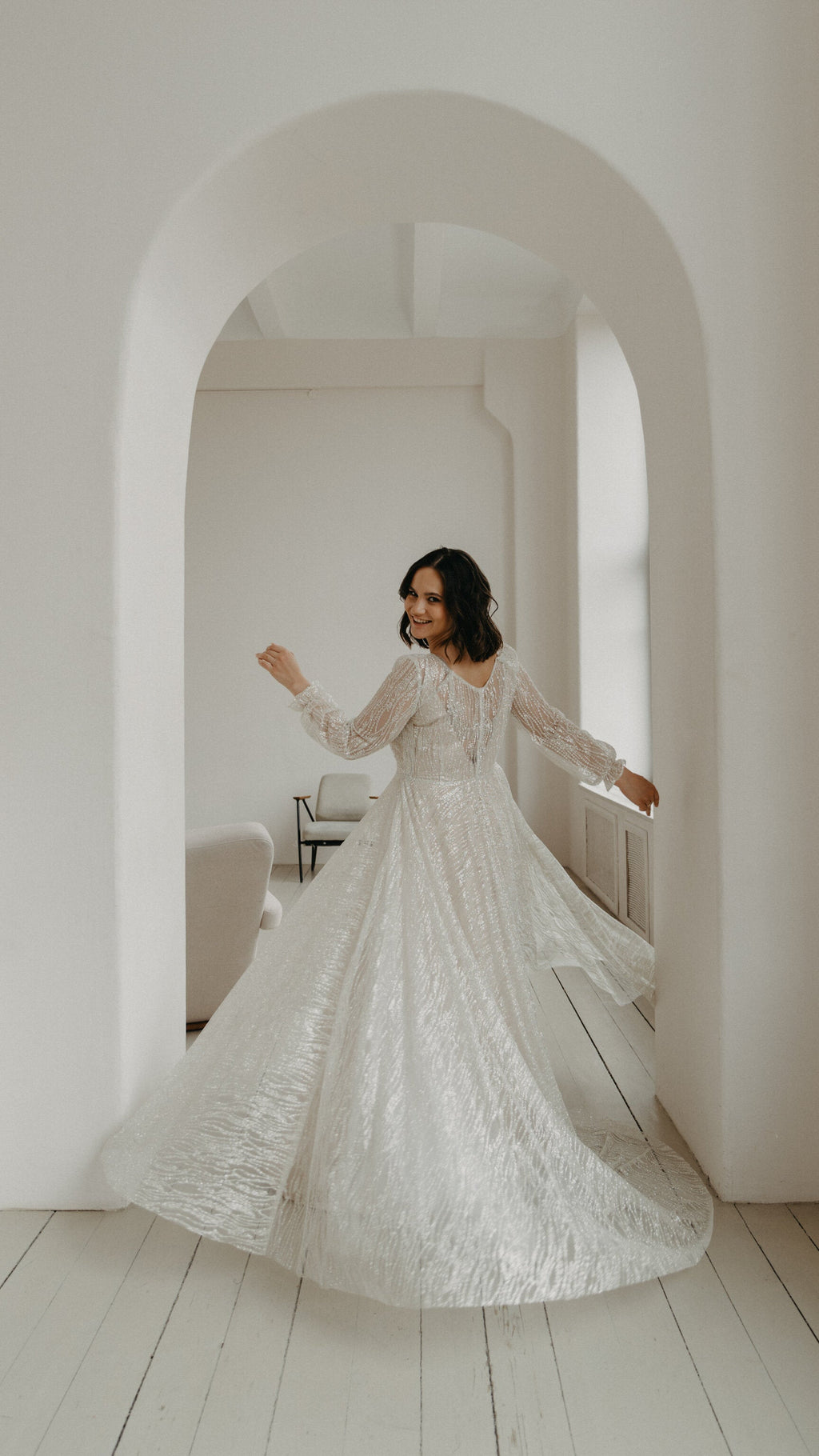 Bride twirling in a white arched room, full A-line skirt of a pale glitter lace wedding dress spreading wide, Galaxy Champagne