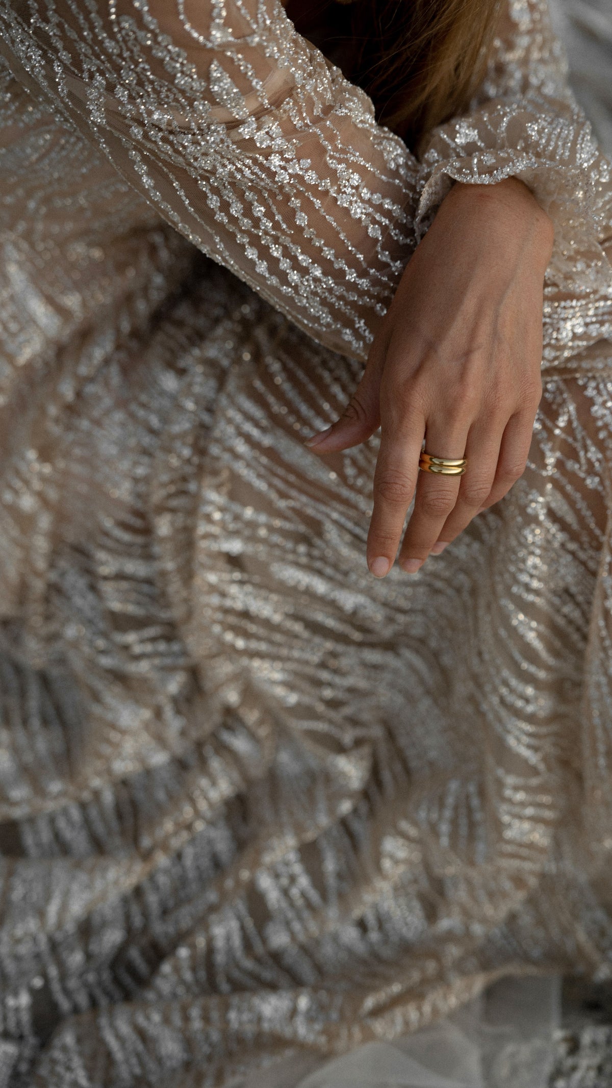 Macro of silvery glitter lace swirls on the sleeve and skirt of a champagne wedding dress, hand with a gold ring, Galaxy Champagne