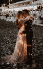 Couple kissing on a night beach, string lights tucked into the train of a champagne glitter lace wedding dress, beach club behind, Galaxy Champagne