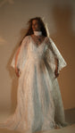 Two-piece celestial wedding dress in ivory glitter lace with flowing open sleeves and a V neckline, warm studio light. Galaxy Ivory 2.0 by Ephemeris