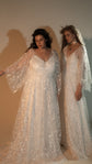 Two models side by side, a star lace wedding dress with flutter sleeves and an ivory glitter lace wedding dress with a neck scarf, Galaxy Ivory 2.0