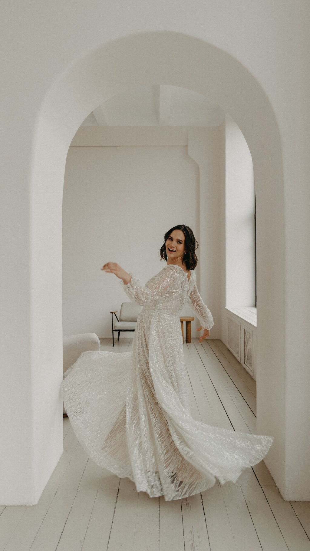 Bride laughing as she twirls under a white arch, side view of an ivory glitter lace wedding dress with a swirling skirt, Galaxy Ivory Sample