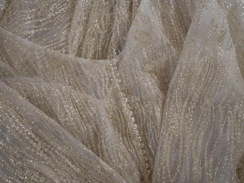 Fabric detail of ivory glitter lace with wavy gold-toned threads and a row of small buttons on the sample wedding dress, Galaxy Ivory Sample