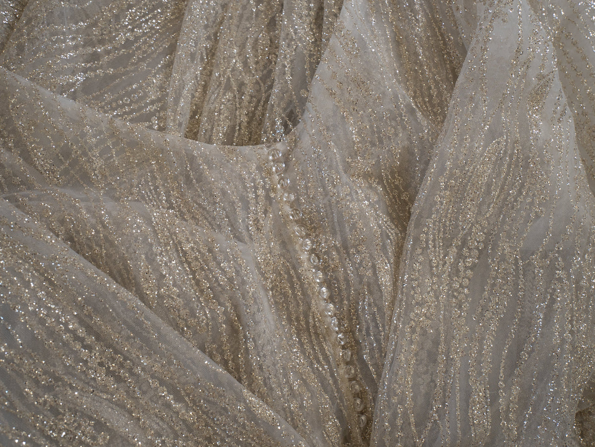 Fabric detail of ivory glitter lace with wavy gold-toned threads and a row of small buttons on the sample wedding dress, Galaxy Ivory Sample