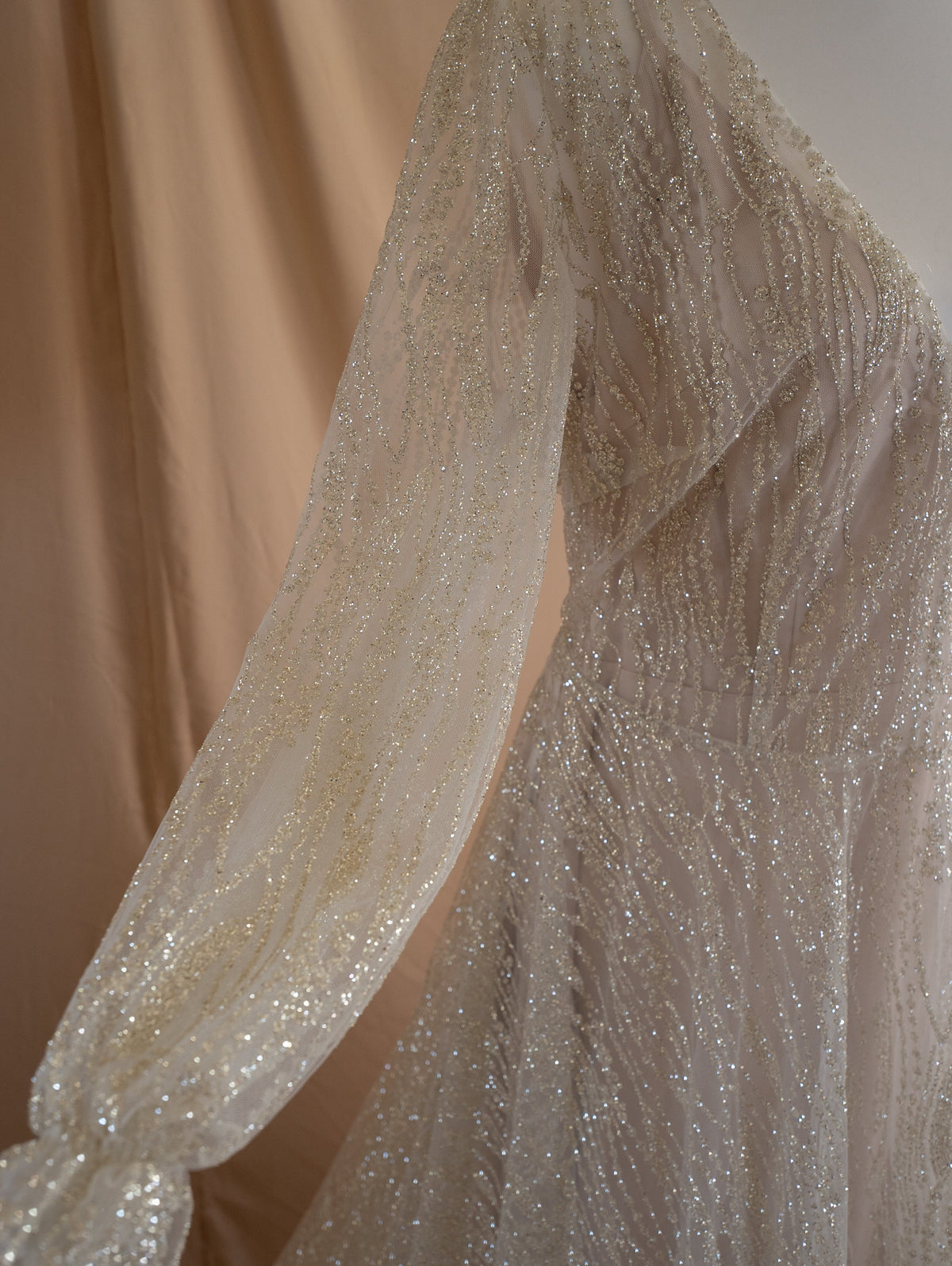 Close-up of a sheer glitter lace sleeve with a gathered cuff and the V-neck bodice of an ivory wedding dress, Galaxy Ivory Sample