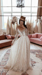 Ivory glitter lace wedding dress with a V neckline and sheer long sleeves, bride taking a mirror selfie in a bridal showroom. Galaxy Ivory by Ephemeris