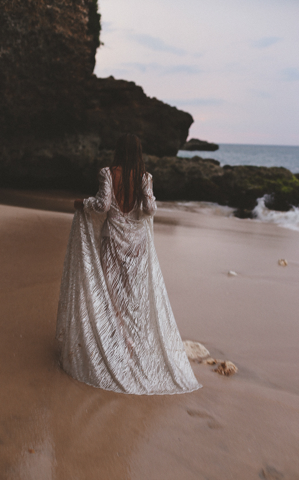 Rear view of an ivory glitter lace wedding dress with an open back, bride holding the train at the water edge, Galaxy Ivory