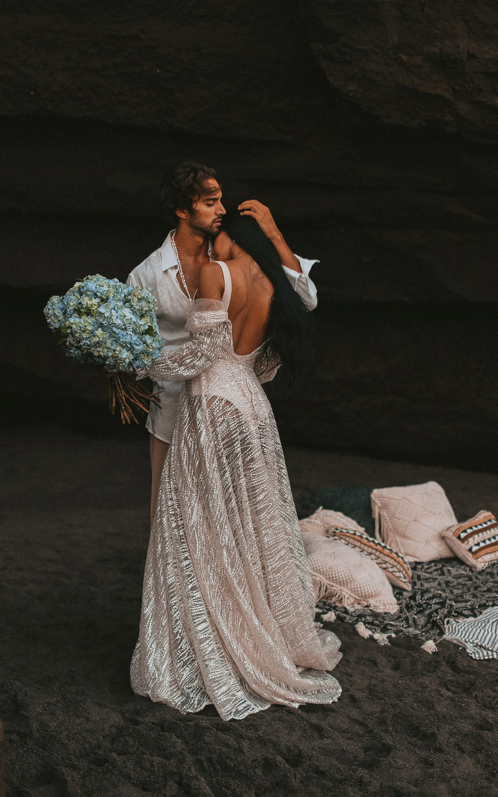 Groom kissing the bride shoulder in a dark cave, open back and sheer skirt of an ivory glitter lace wedding dress, Galaxy Ivory