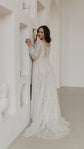 Bride leaning on a sculpted white wall, back view of an ivory lace wedding dress with a scoop back and buttons, Galaxy Ivory