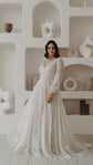 Front view of a V-neck ivory lace wedding dress with gathered cuffs before white shelves of ceramic vases, Galaxy Ivory