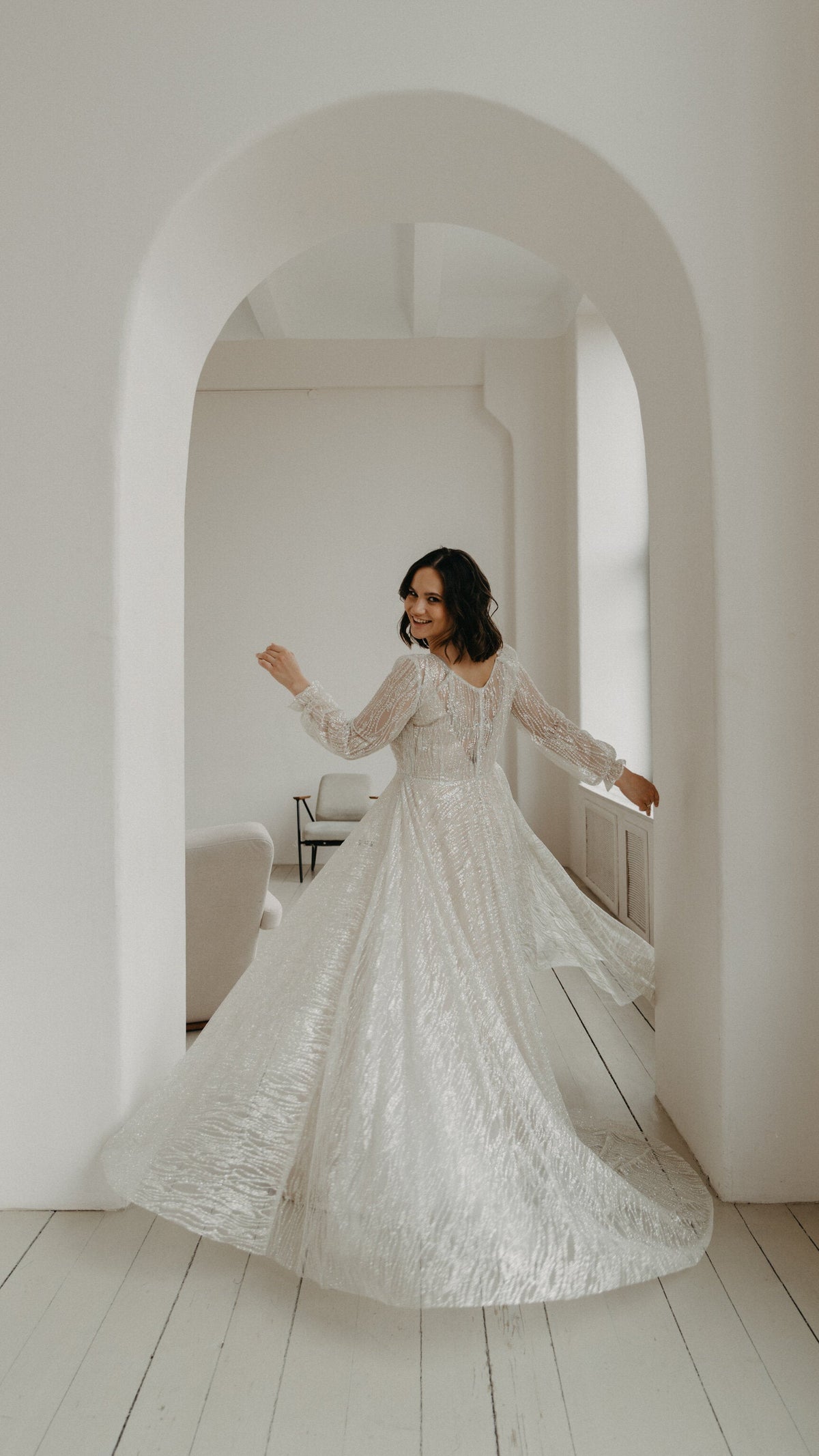 Back view of a bride dancing in a white archway, buttoned back of an ivory lace wedding dress and a wide swirling skirt, Galaxy Ivory