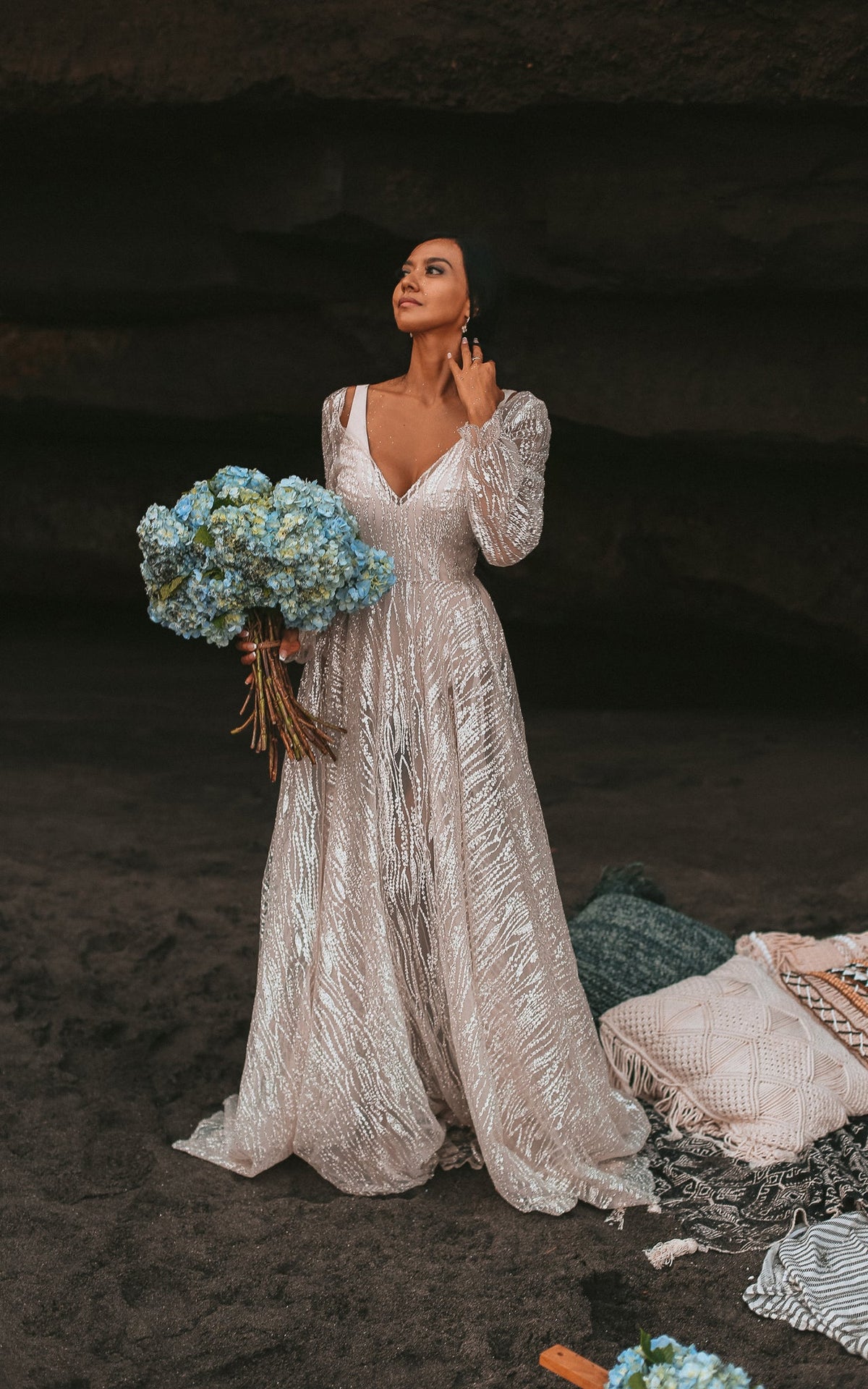 Boho bride in a sea cave holding blue hydrangeas, V-neck ivory glitter lace wedding dress with puffed sleeves, Galaxy Ivory