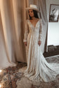 Ivory lace wedding dress with a deep V neckline and long cuffed sleeves, bride in a wide-brim hat on a patterned rug, Galaxy Ivory