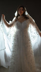 Model spreading a backlit hooded bridal cape wide over a star tulle wedding dress, lace stars along the trim, Holly Cape