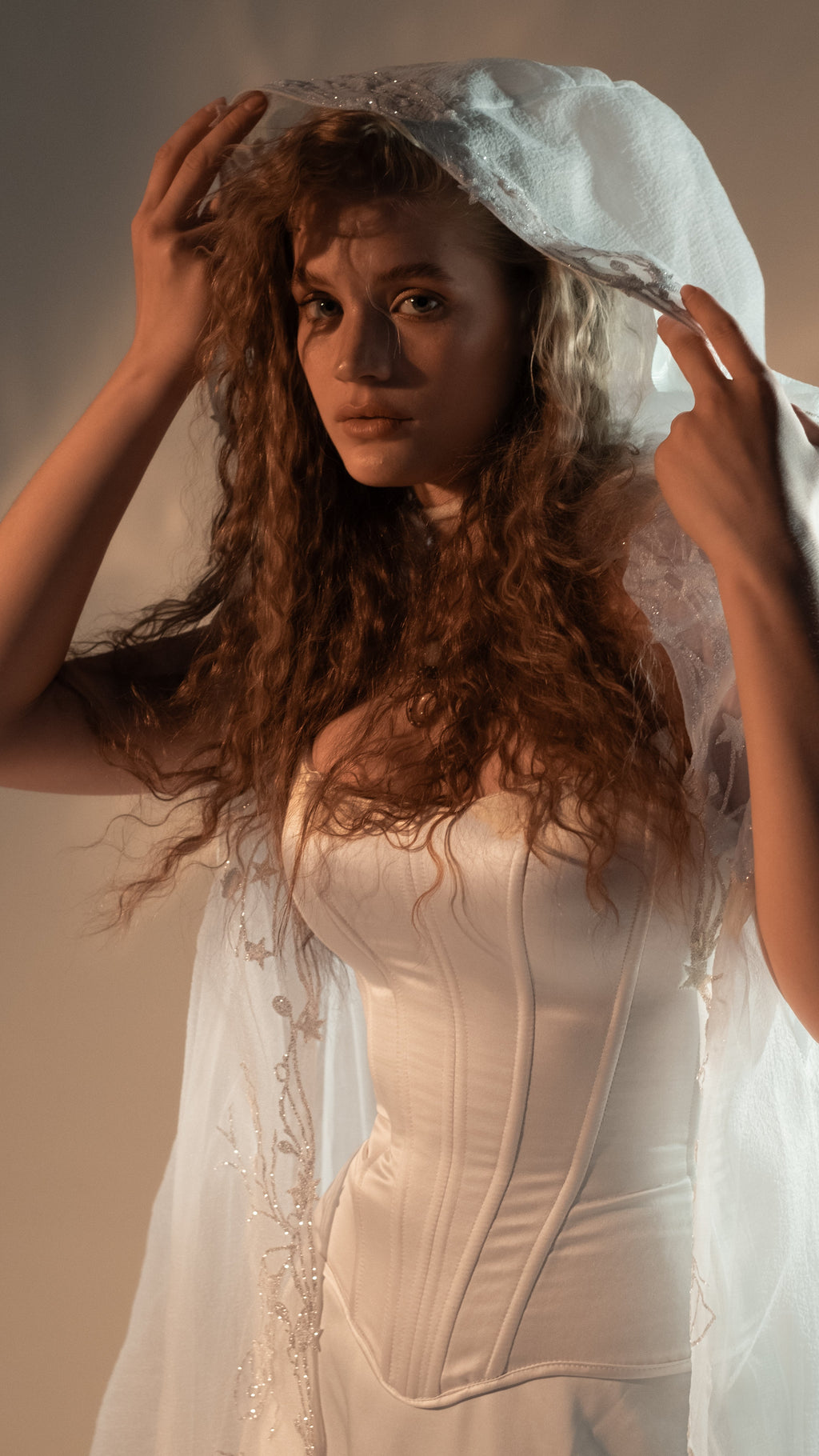 Model holding the hood of an ivory chiffon bridal cape above her head, beaded star vine lace down the front, Holly Cape