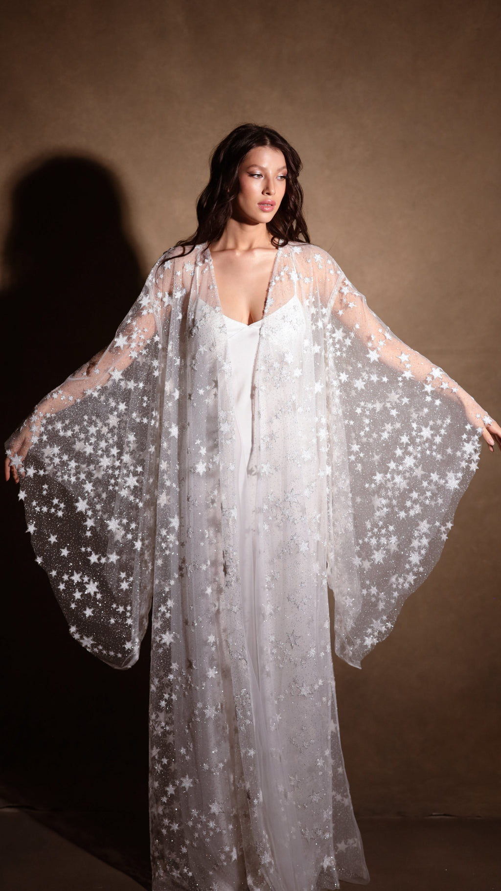 Long bridal slip dress in ivory with thin straps, worn under a sheer star tulle robe with wide sleeves. Infinity Slip Ivory by Ephemeris