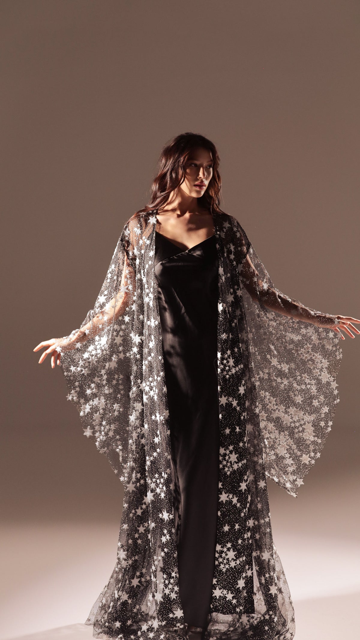 Black version of the long slip dress under a black star tulle robe, model with arms spread in studio light, Infinity Slip Ivory
