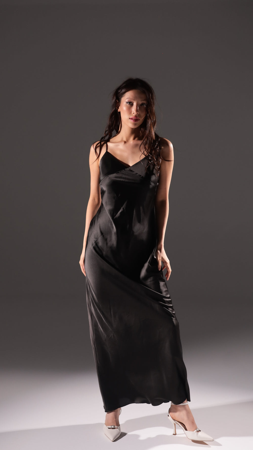 Black long slip dress with a V neckline and thin straps, shown as the second colour option, white heels, Infinity Slip Ivory
