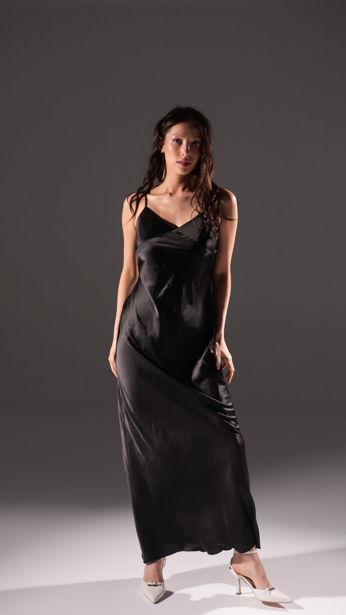 Black long slip dress with a V neckline and thin straps, shown as the second colour option, white heels, Infinity Slip Ivory