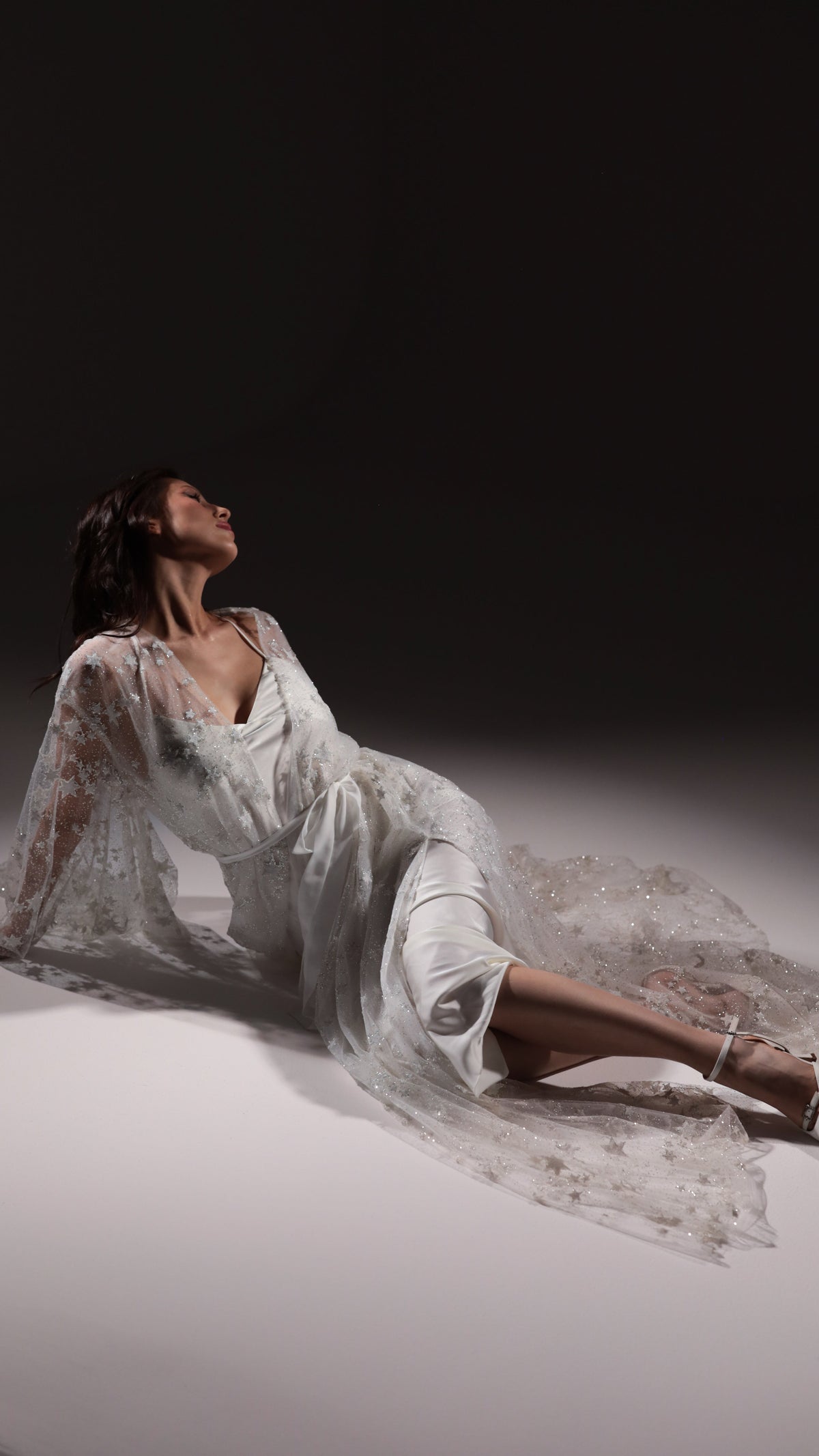 Model reclining on the floor in an ivory slip dress under a star embellished tulle robe spread around her, Infinity Slip Ivory