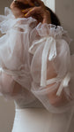 Close-up of crinkled organza bridal sleeves gathered with ribbon bows and ruffled elastic cuffs, hand raised, LUNA Sleeves
