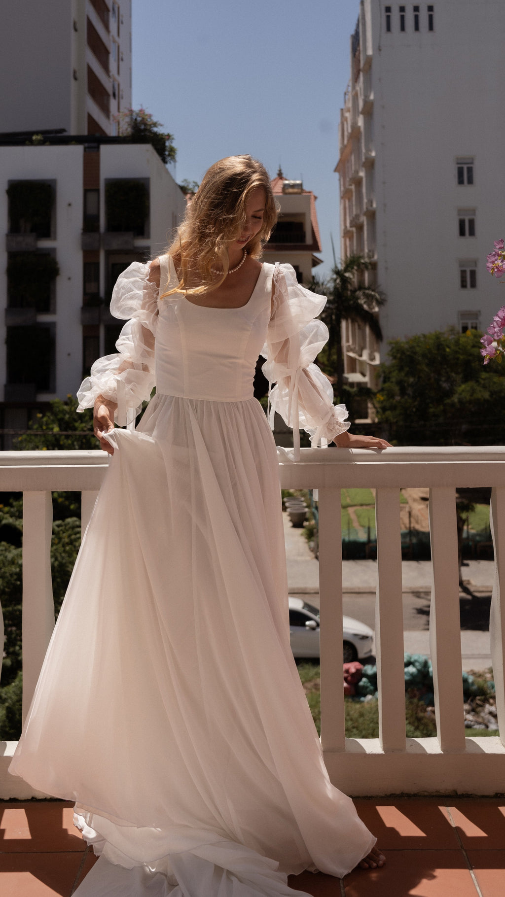 Off-shoulder organza bridal sleeves with ruffles and fluttering ribbons over a square-neck gown, bride on a balcony, LUNA Sleeves