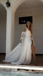 Barefoot bride in sunglasses at a poolside arch, chiffon wedding dress with a leg slit and ribbon-tied sleeves, rose in hand, LUNA