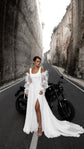 Front view on a canyon road of a minimalist chiffon wedding dress with off-shoulder organza sleeves and a thigh slit, motorbike behind, LUNA