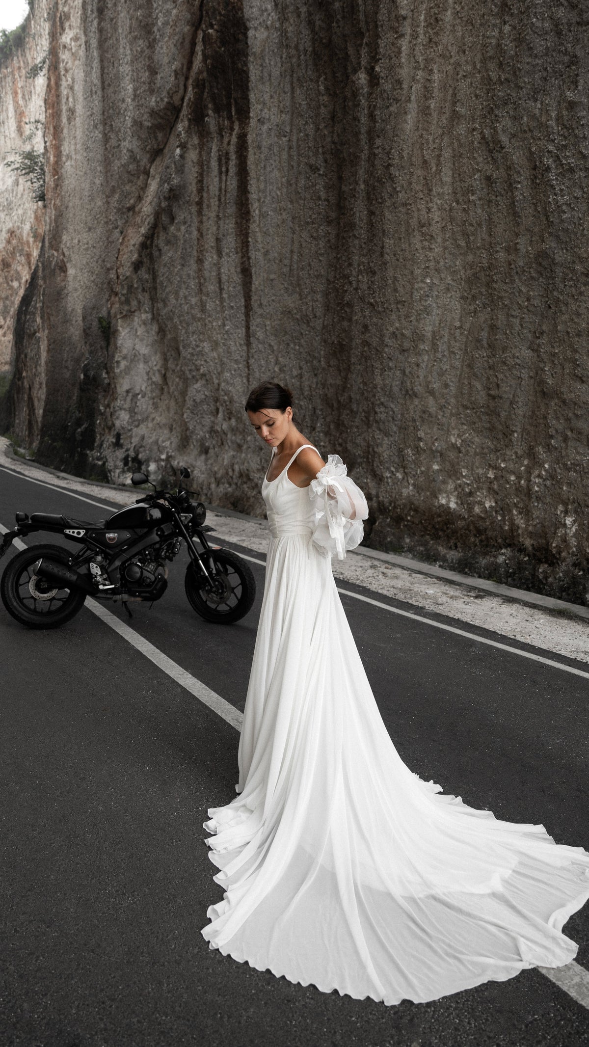 Bride walking along a canyon road, long chiffon train of a square-neck wedding dress trailing behind, motorbike parked, LUNA