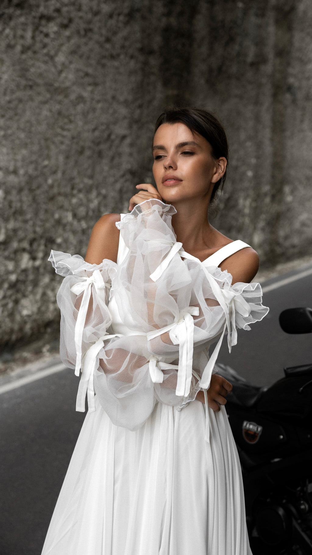 Bride with hands near her chin wearing layered organza puff sleeves with bows over a sleeveless chiffon wedding dress, LUNA