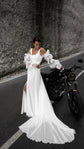 Bride resting a hand on a motorbike, chiffon wedding dress with off-shoulder sleeves and a train spread across the lane line, LUNA