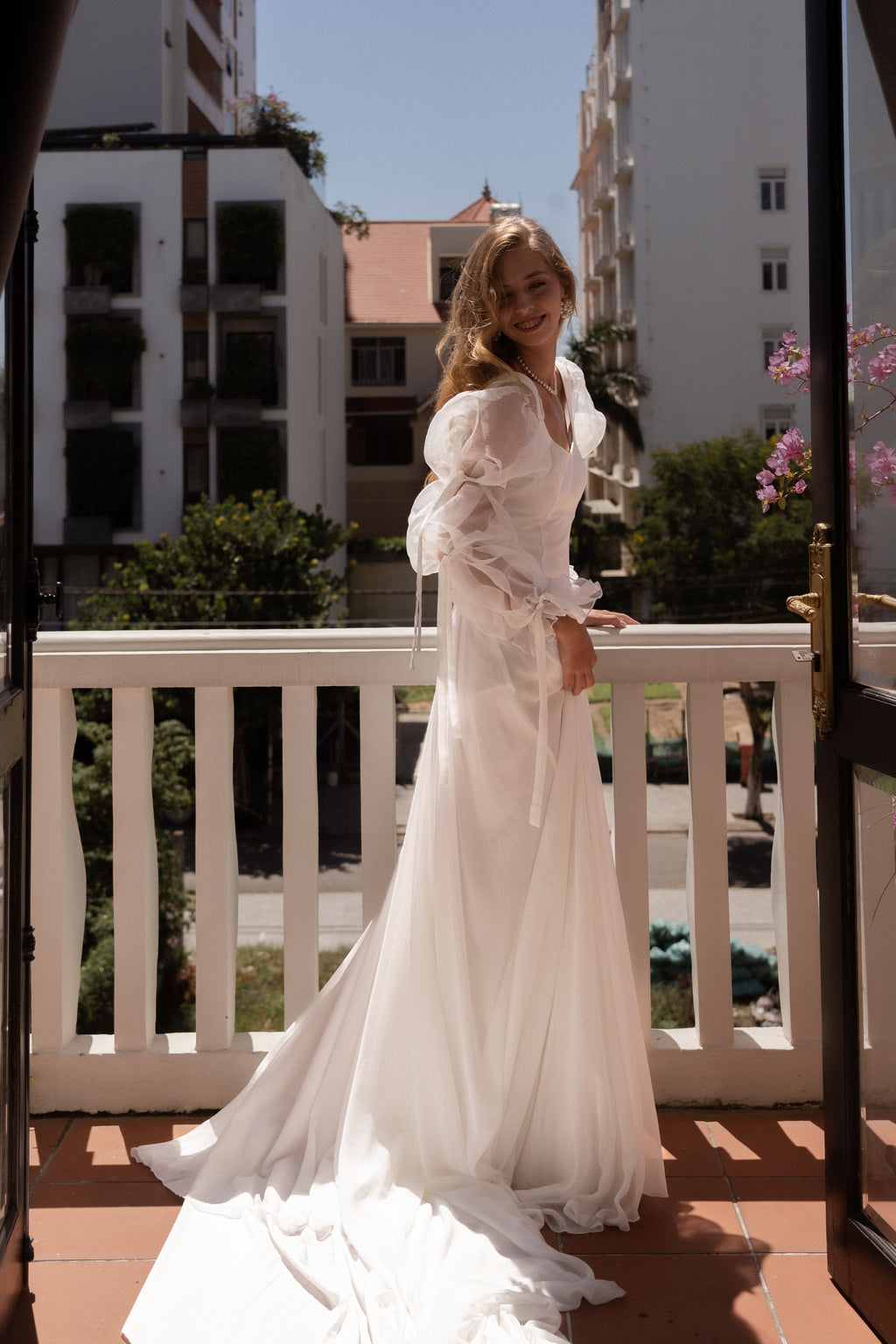 Smiling bride on a sunny balcony, A-line chiffon wedding dress with sheer organza sleeves and a train across the tiles, LUNA