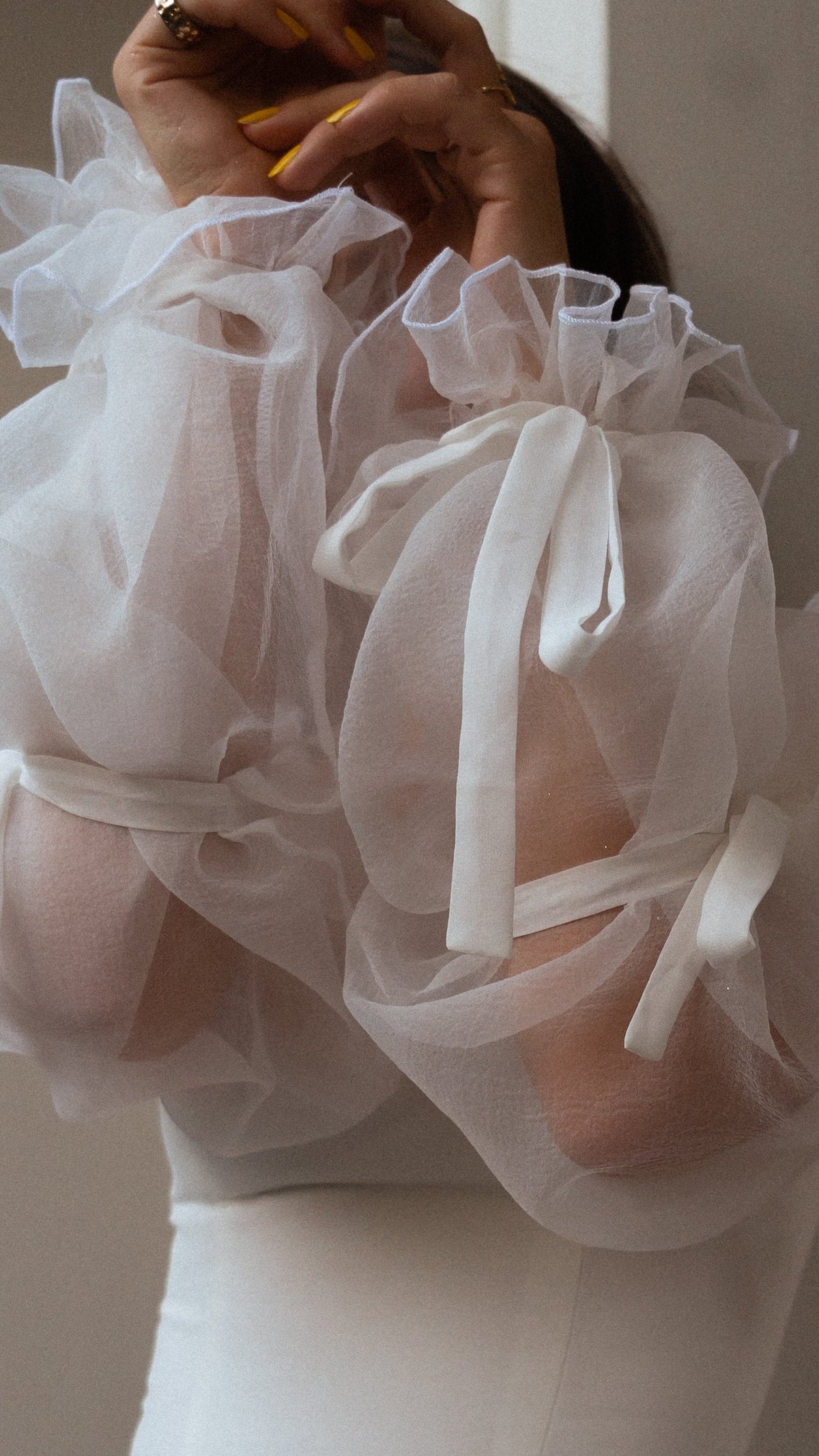 Close-up of crinkled organza puff sleeves with ruffled cuffs and ribbon bows, hand raised, on a chiffon wedding dress, LUNA