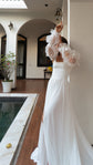 Bride stretching up against a pillar by a courtyard pool, square-neck wedding dress with off-shoulder organza sleeves, LUNA