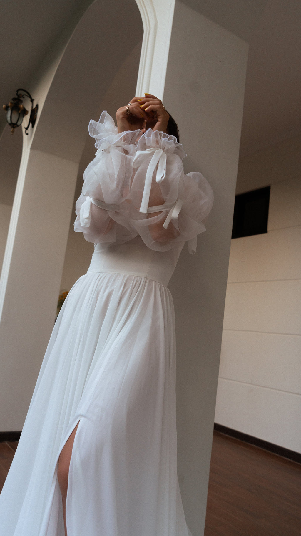Low-angle crop of ruffled organza sleeves raised overhead and a gathered chiffon wedding dress skirt with a slit, LUNA