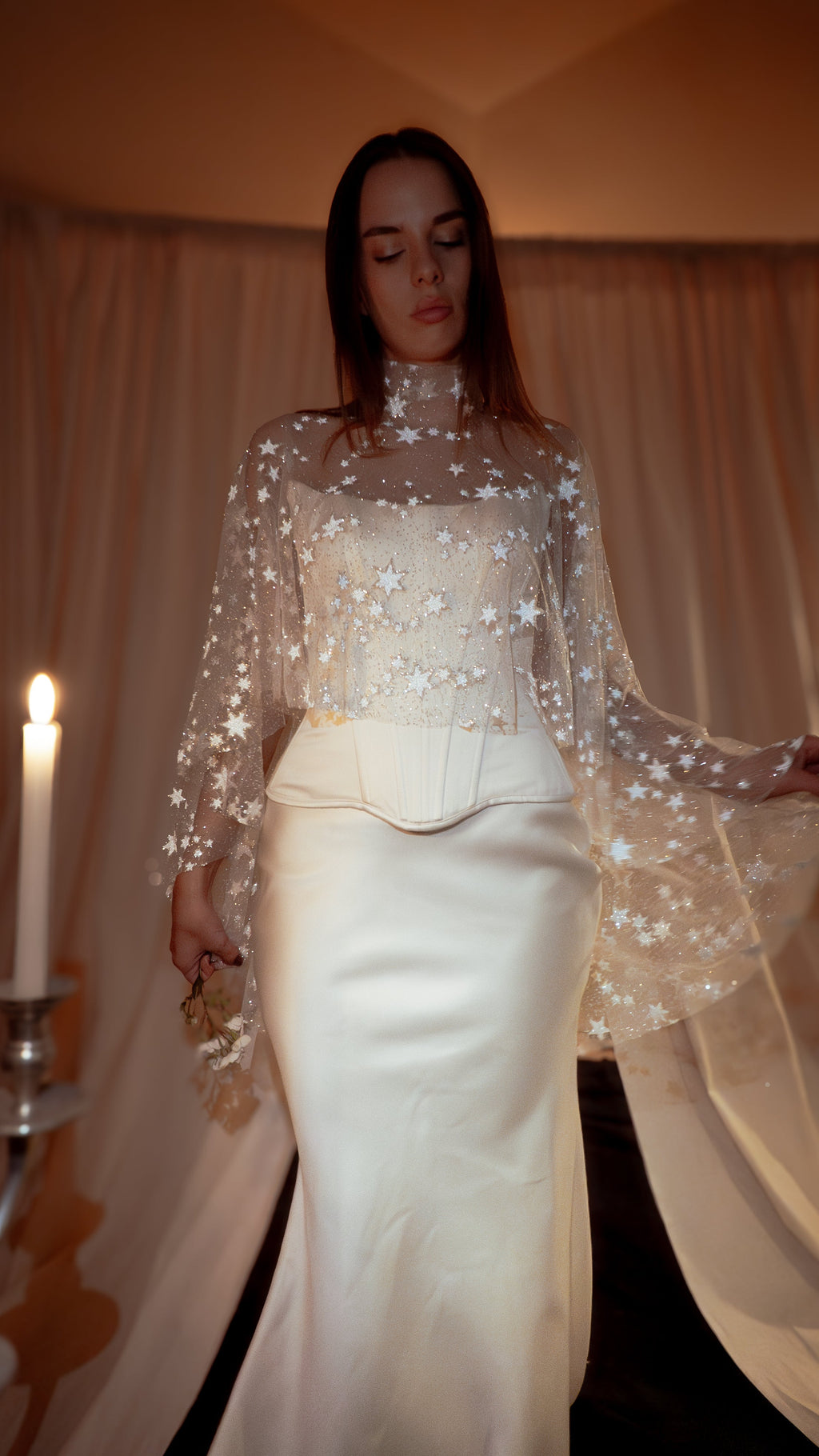Celestial bridal cape in sheer star tulle with a high neck, draped over a corset and satin skirt by candlelight. Lunar Eclipse Cape Ivory by Ephemeris