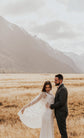 Elopement couple in a golden grass valley under mountains, bride holding out the edge of a star bridal cape, Lunar Eclipse Cape Ivory
