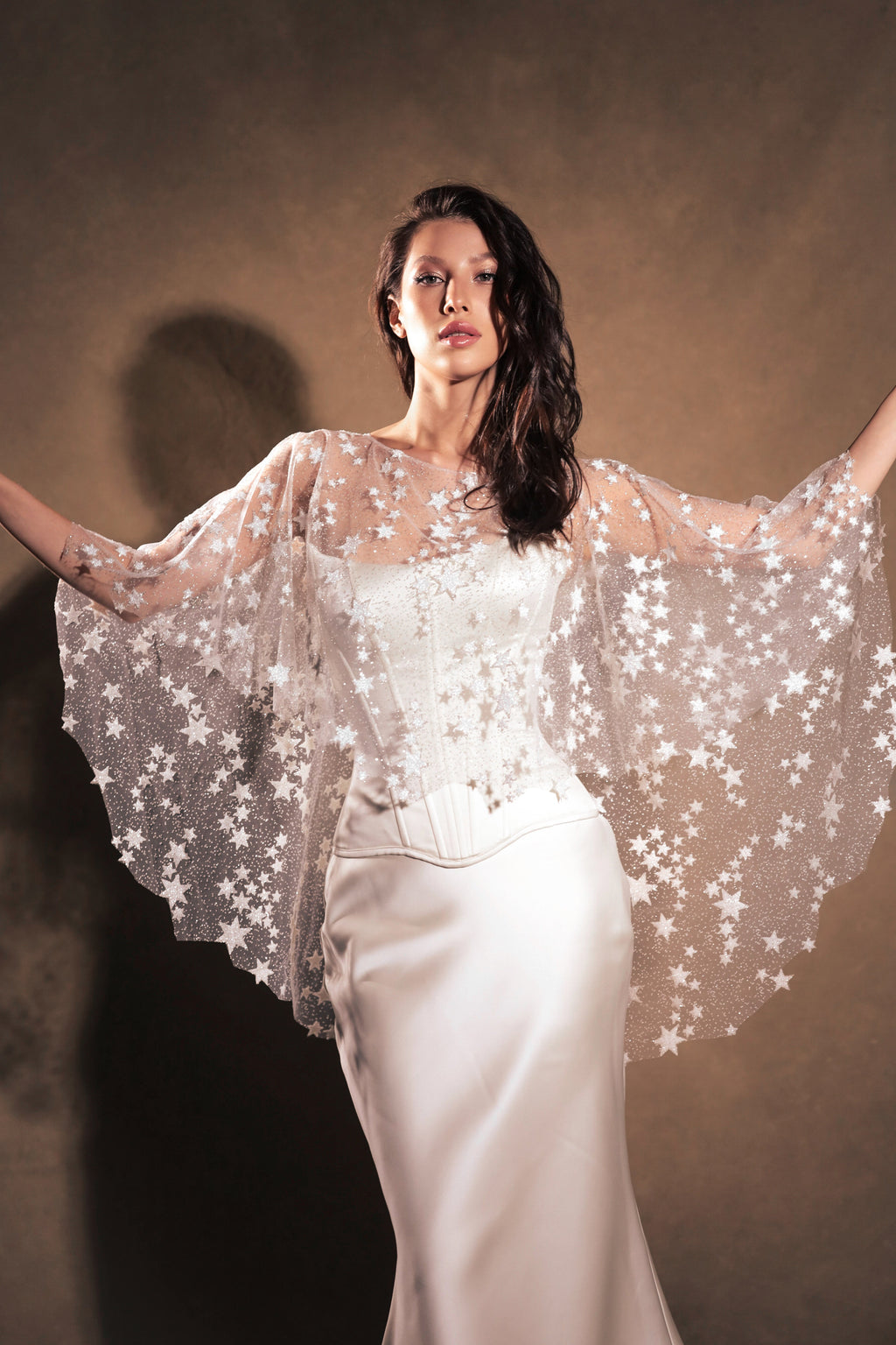 Model spreading her arms to show the round shape of a star tulle bridal cape over a corset gown, Lunar Eclipse Cape Ivory