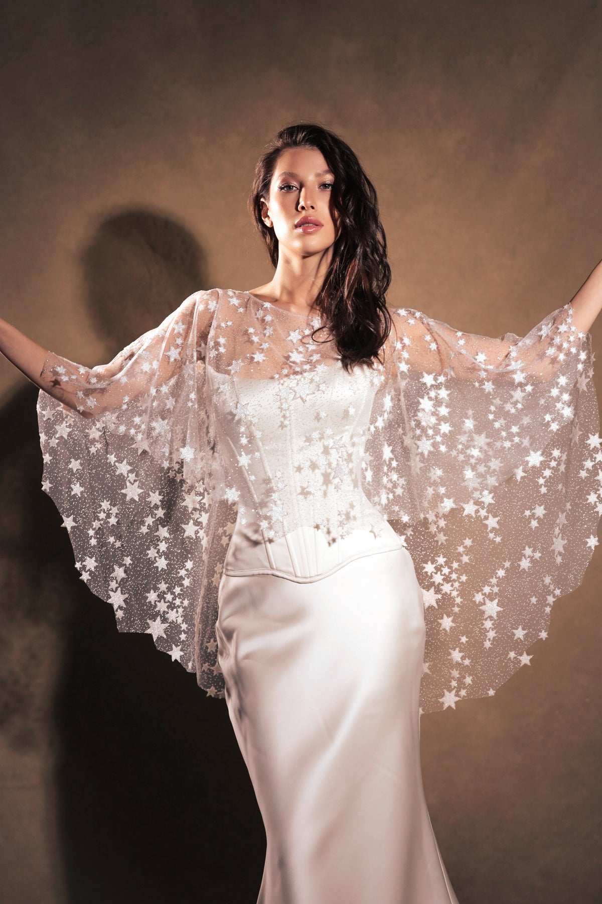 Model spreading her arms to show the round shape of a star tulle bridal cape over a corset gown, Lunar Eclipse Cape Ivory